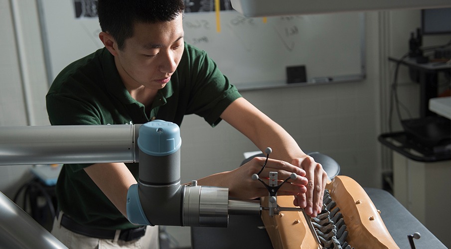 Male student working with a robotic arm in the lab.