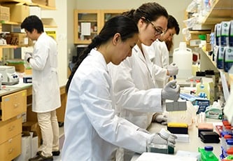 Two female students are wearing white coats and working in a wet lab.