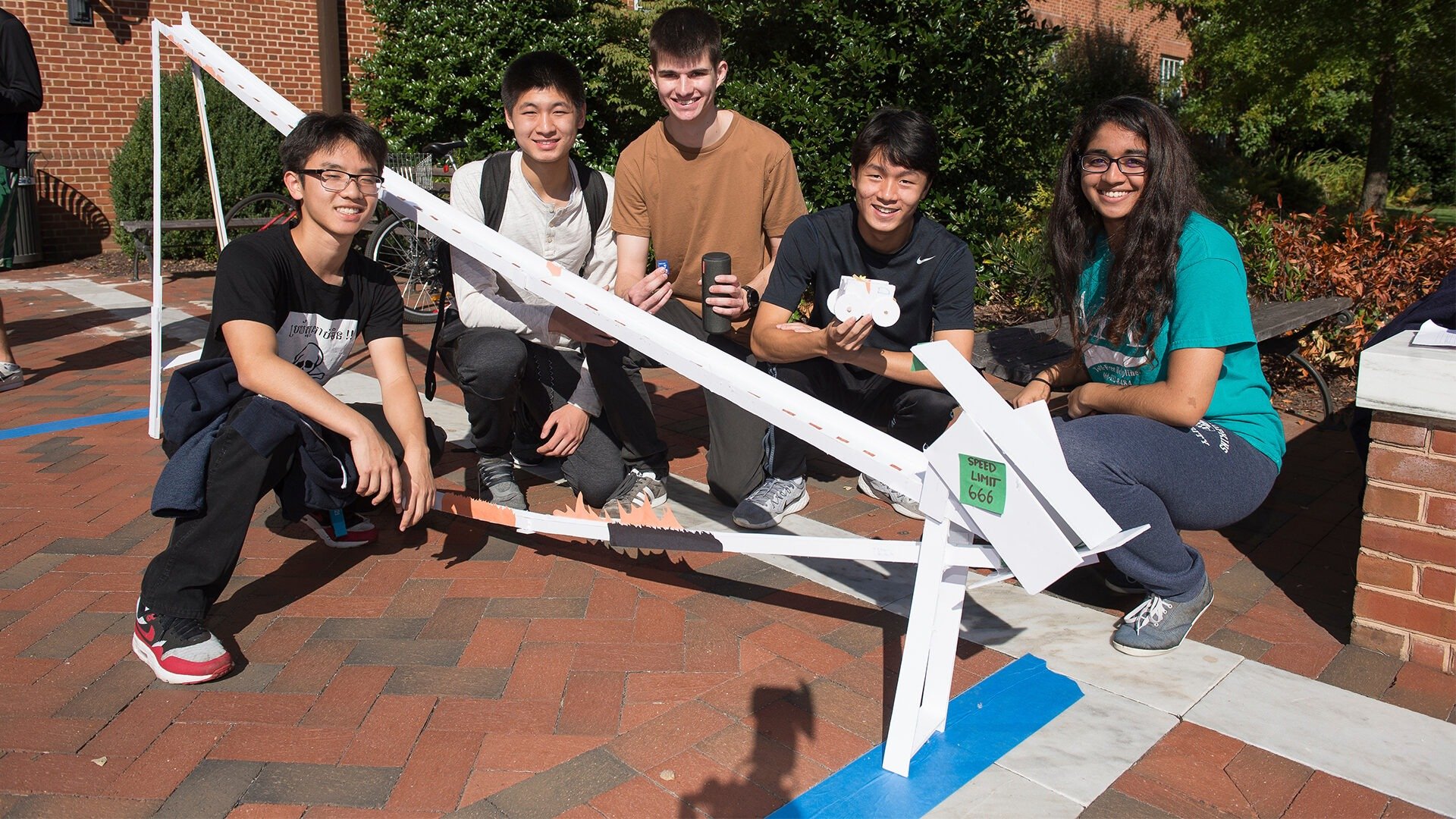 A group of students pose outside with their foam-core roller coaster design.