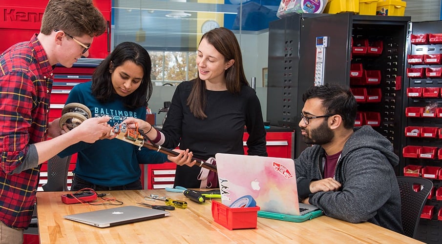 Three students work with a faculty member at a table in the Design Studio on a prototype.