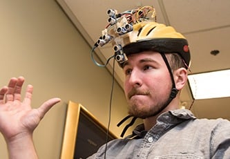 Student poses wearing a helmet prototype he and his teammates designed.