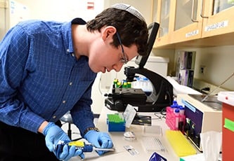 A young student works in a wet lab using a pipette.