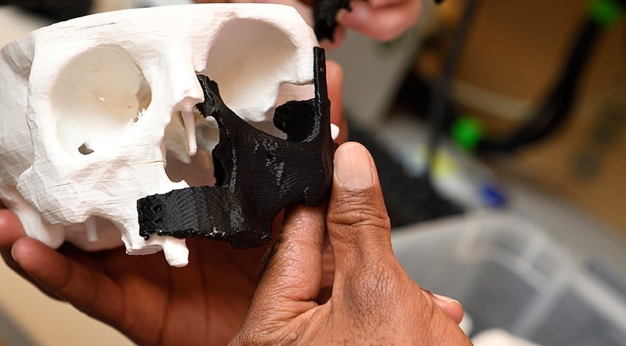 A set of hands hold up a 3-D printed human skull.