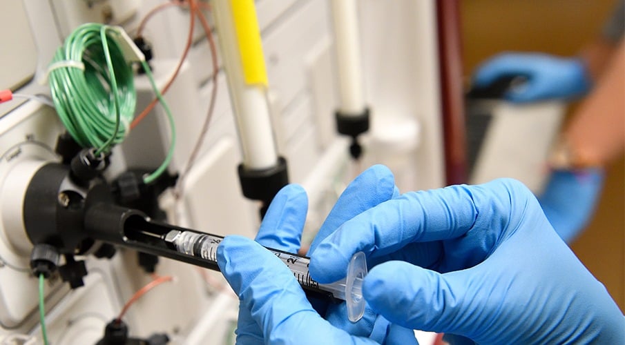 This close-up shot shows gloved hands working with a piece of equipment in the lab.