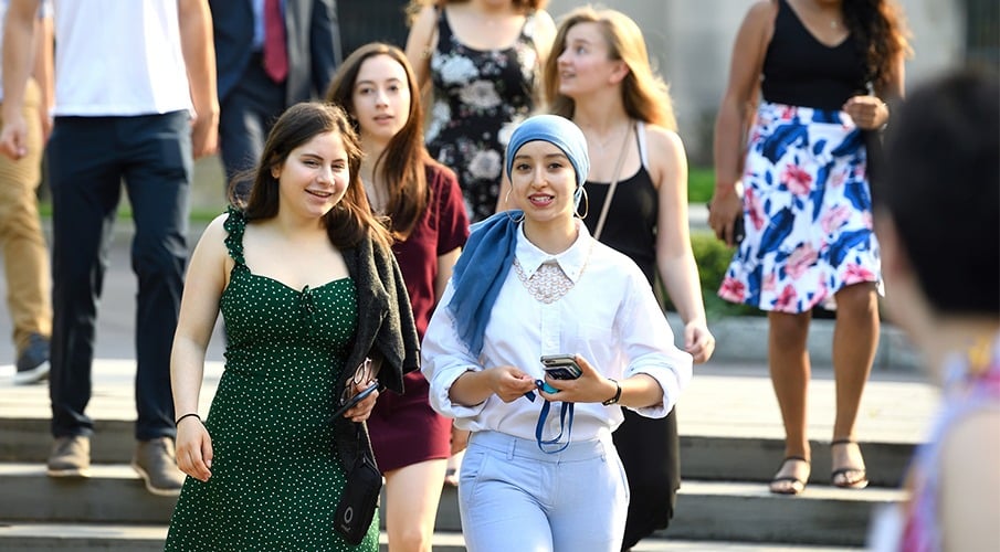 A group of students walk down a set of stairs outside talking and smiling.