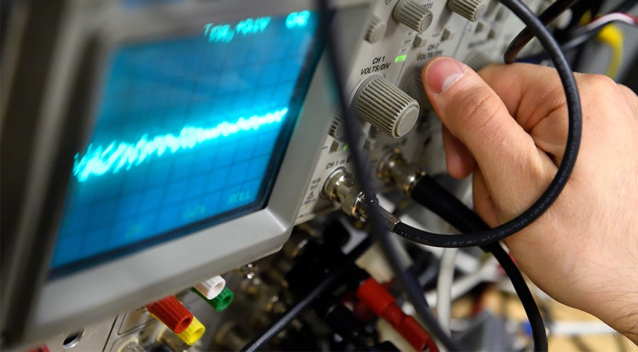 A hand reaches to adjust a dial on a machine with a screen and many wires.