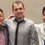 The three male students stand together and smile.