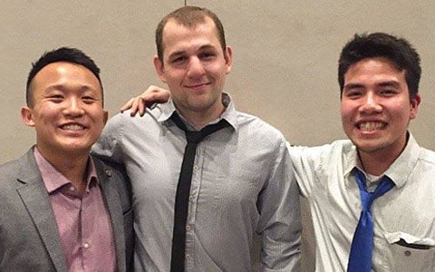 The three male students stand together and smile.