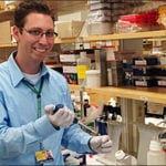 Jordan Green smiles at the camera while pipetting in the lab.