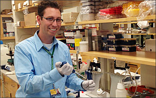 Jordan Green smiles at the camera while pipetting in the lab.