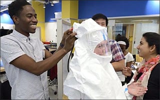 Student help another student try on a white ebola suit.