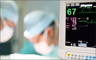 A clinicial is working in the background and a patient monitor is in the foreground.