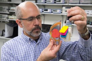 Juan Garcia holds up some colorful 3-d printed objects.