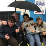 The students pose with a boy in a wheelchair with a prototype of their retractable umbrella.