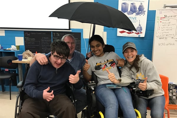 The students pose with a boy in a wheelchair with a prototype of their retractable umbrella.