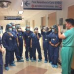 Students wear scrubs and talk with a clinician in the hall of the hospital.