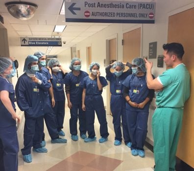 Students wear scrubs and talk with a clinician in the hall of the hospital.