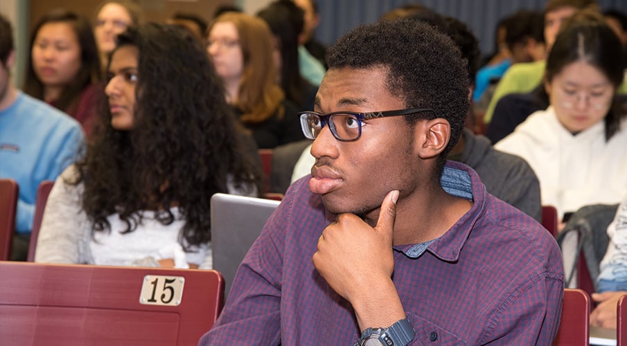 An African-American male student sits in a lecture hall and listens.