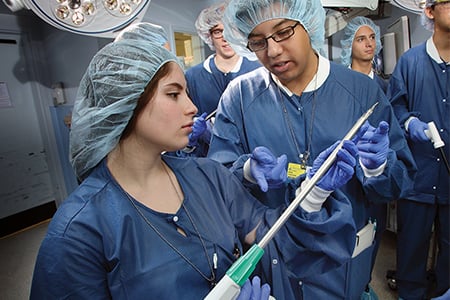 A female undergraduate student holds up a medical device in the operating room to discuss with a fellow student.