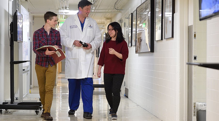 Two students walk down the hall with a clinician while discussing a project.