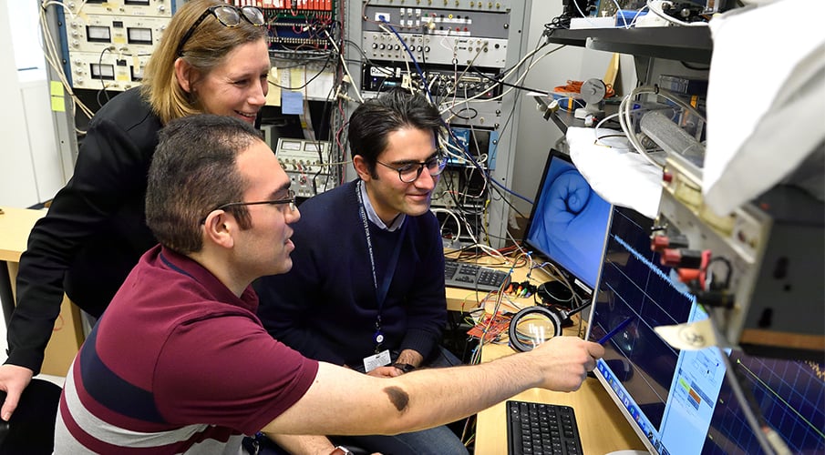 Two male students work at a computer with a female professor.