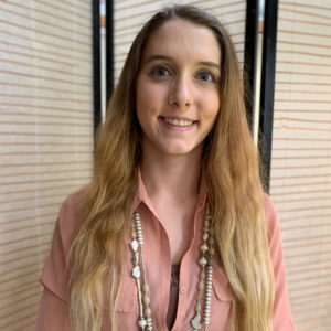 Sophia Doerr smiles for the camera wearing a pink shirt and a white necklace.