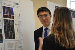 A male student stands near his poster to present his research.