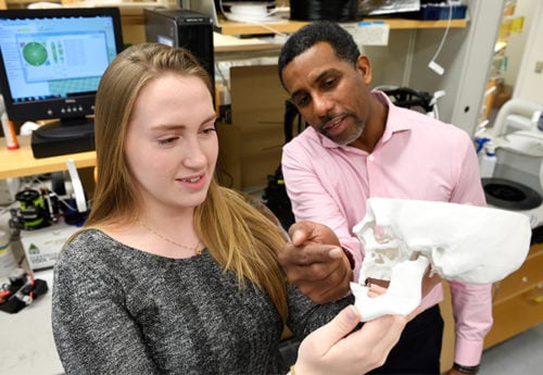 A student and faculty member talk while holding up a 3D printed human skull.