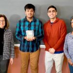 Three BME students stand with a teacher holding the piece of scrap metal.