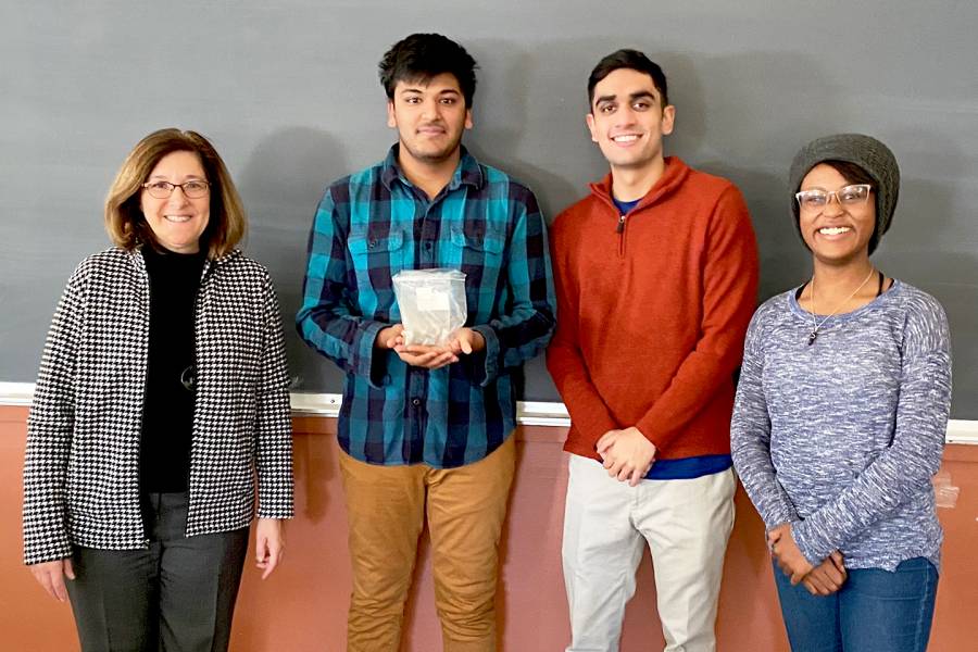 Three BME students stand with a teacher holding the piece of scrap metal.