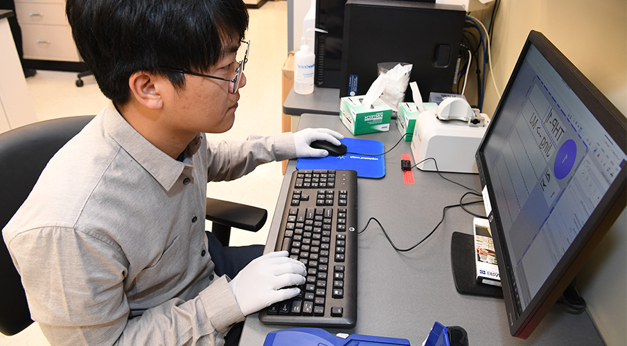 A male student works at a computer in a lab wearing gloves.