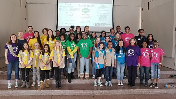 The group of girl scouts and their mentors stand on the stage for a photo.