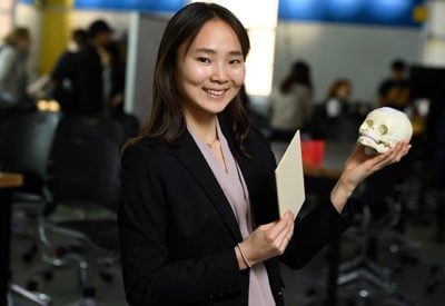 A female student holds a model of the human skull while smiling at the camera.