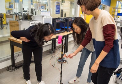 Three female students work in the Design Studio on their smart cane prototype.