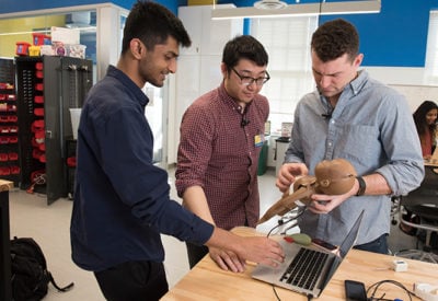 Three male students work on their prototype with a doll and a laptop.