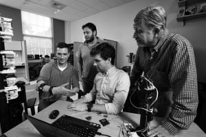 Three students and a professor work in the lab on a prosthetic arm.