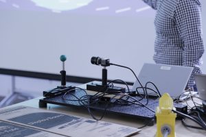 Team one has a device aimed at a small ball on the table.