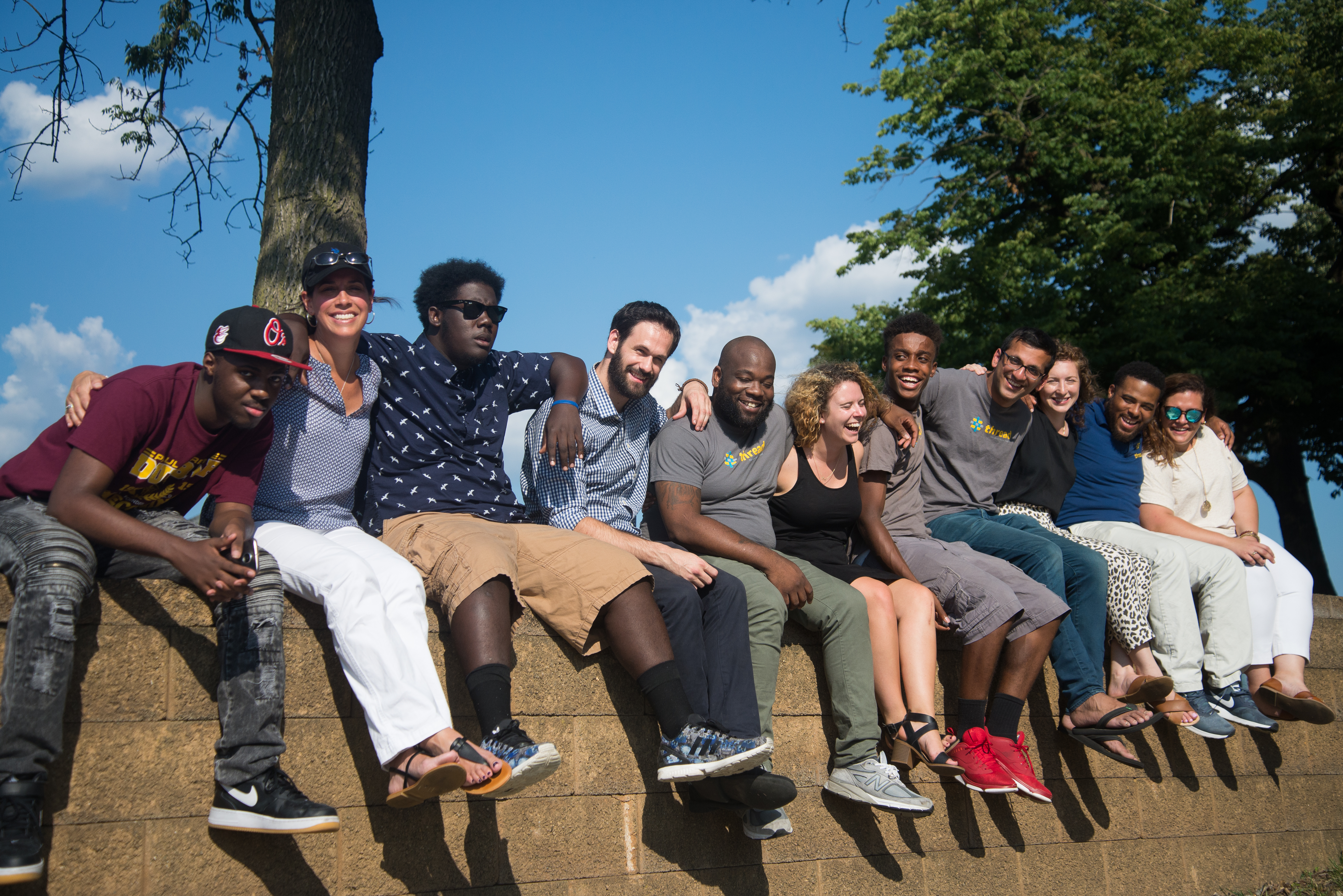 A group of young adults are sitting on a stone wall outside.