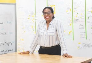 Alina Andrews is standing behind a wood table with a white board in the background.