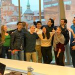 Josh Doloff and the students in his lab gather for a fun group photo in front of windows looking out onto the School of Medicine campus.