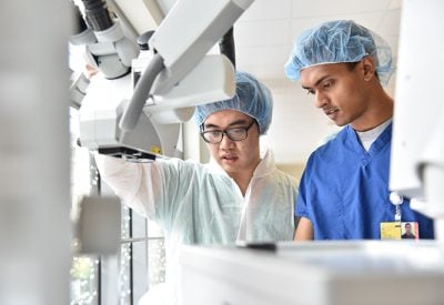 Two males students are in scrubs and working with a medical imaging device.