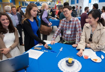 Two alumni talk to two students to discuss a prototype sitting on the table.