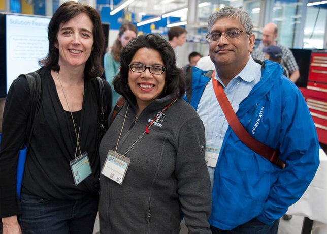 Three alumni stand together and smile for the camera.