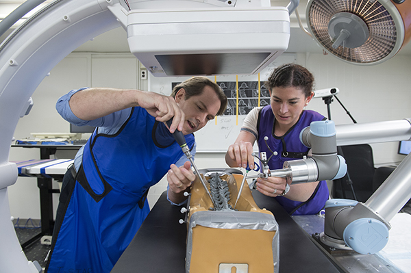 A female student works with a faculty member on a model spine under a medical imaging device.