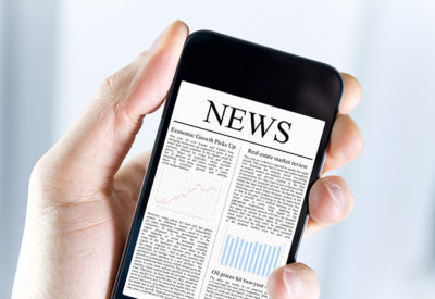 A hand holds a smartphone showing a digital newspaper.