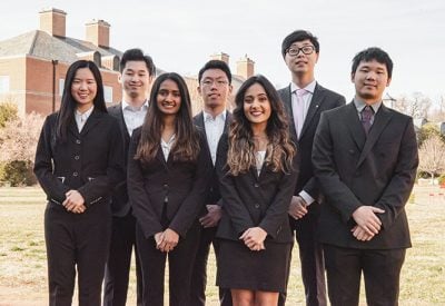 A group of students are dressed professionally and standing together in front of building.