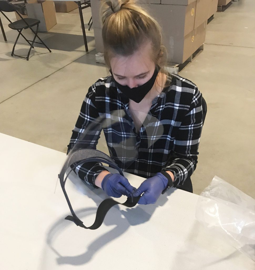 A woman attaches a clear shield and elastic band to the visor.