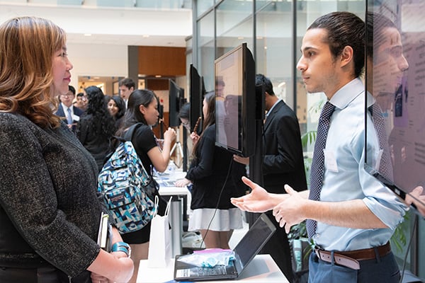 A student speaks with an industry partner in a large room.