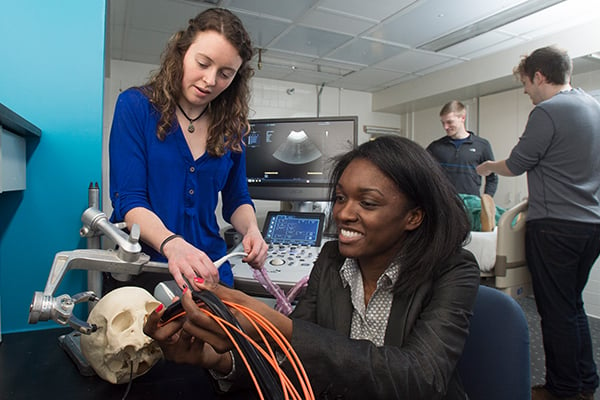 A female student works with a female faculty member on an imaging device and a skull model.