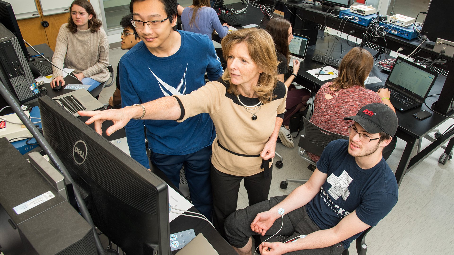 A female faculty member is working with a group of students in a computer lab.